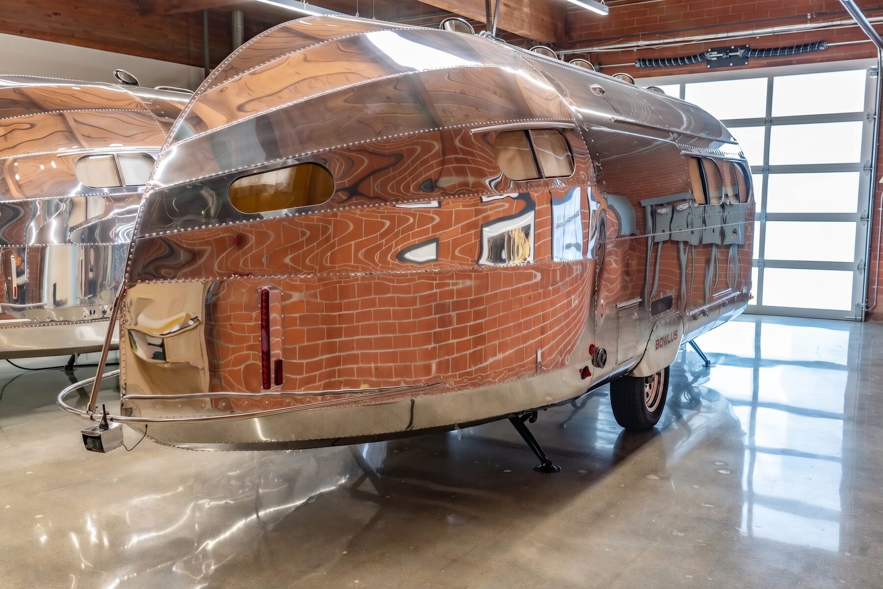 A polished Bowlus travel trailer under a Bowlus nameplate inside the workshop