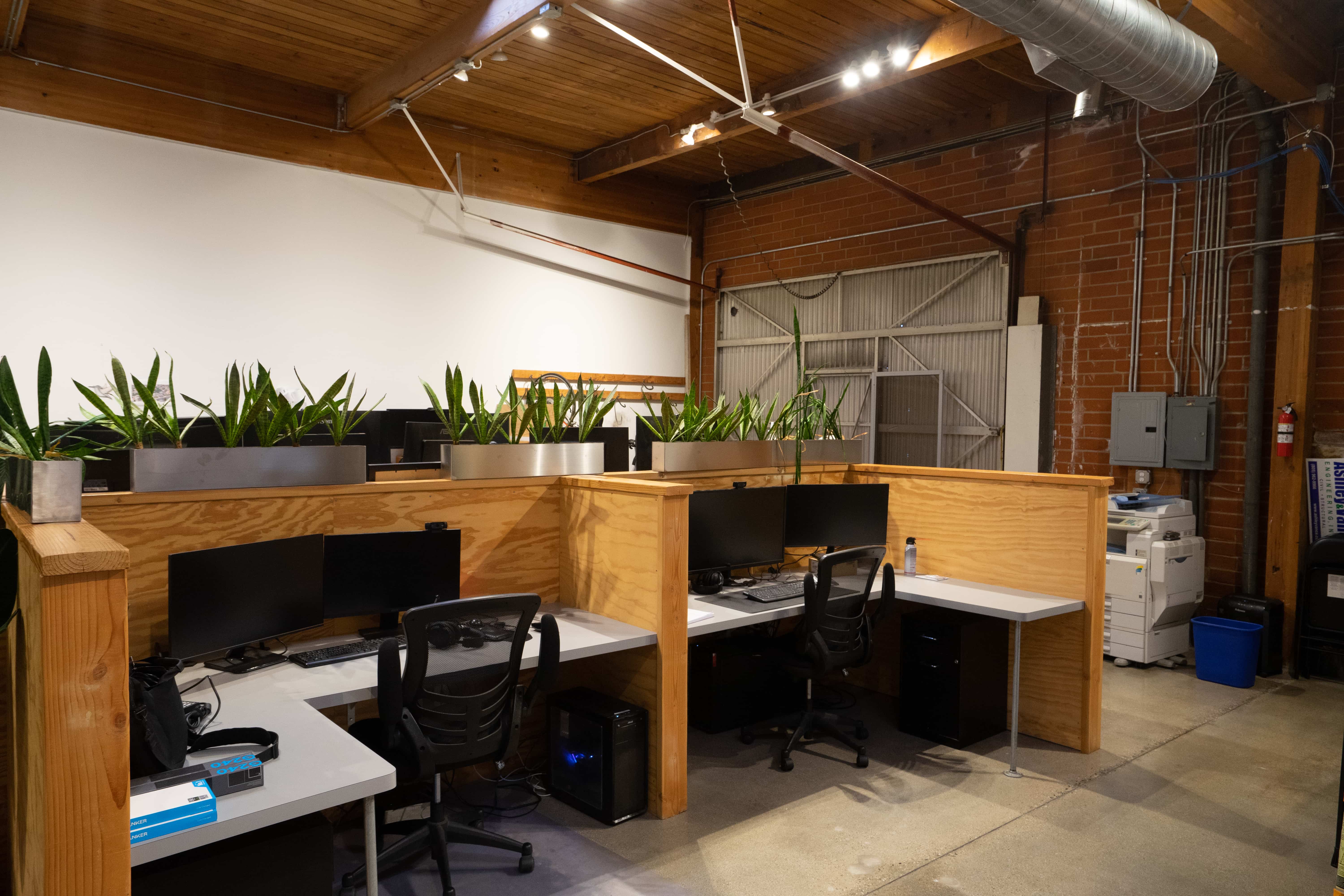 Wood workstations beside an exposed brick wall and roll-up door in Unit 210
